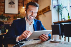 Businessman sitting in cafe looking at tablet during phone call through wireless headphones